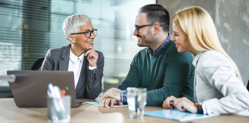 Happy senior agent talking to young couple in the office.