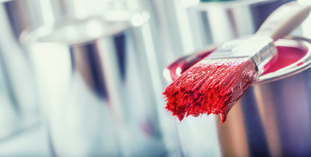 Close-up brush with red color lying on paint can.