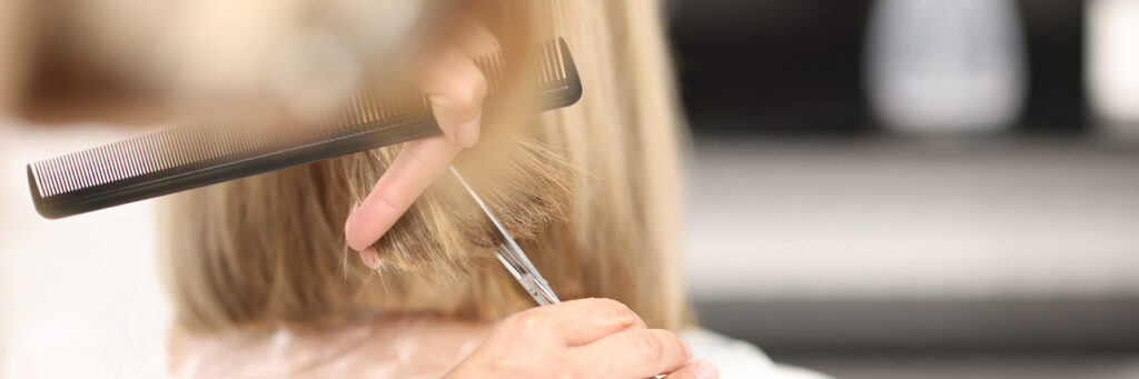 Hairdresser holds comb and scissors in his hands and cuts client’s hair
